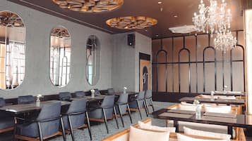 A hotel dining area with multiple tables, chairs, and a chandelier.