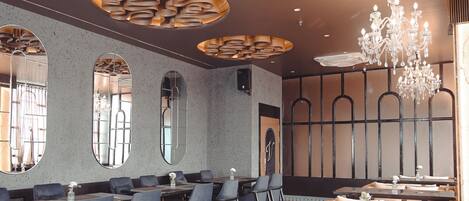A hotel dining area with multiple tables, chairs, and a chandelier.