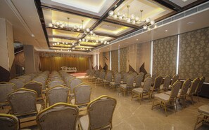 A conference room with rows of chairs, a stage, and a patterned wall. - Dibakar Palace (Tezpur)