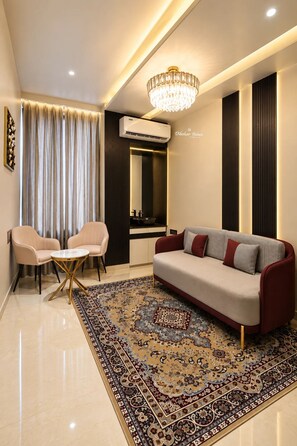 A modern living room with a sofa, two chairs, a chandelier, and a patterned rug. - Dibakar Palace (Tezpur)
