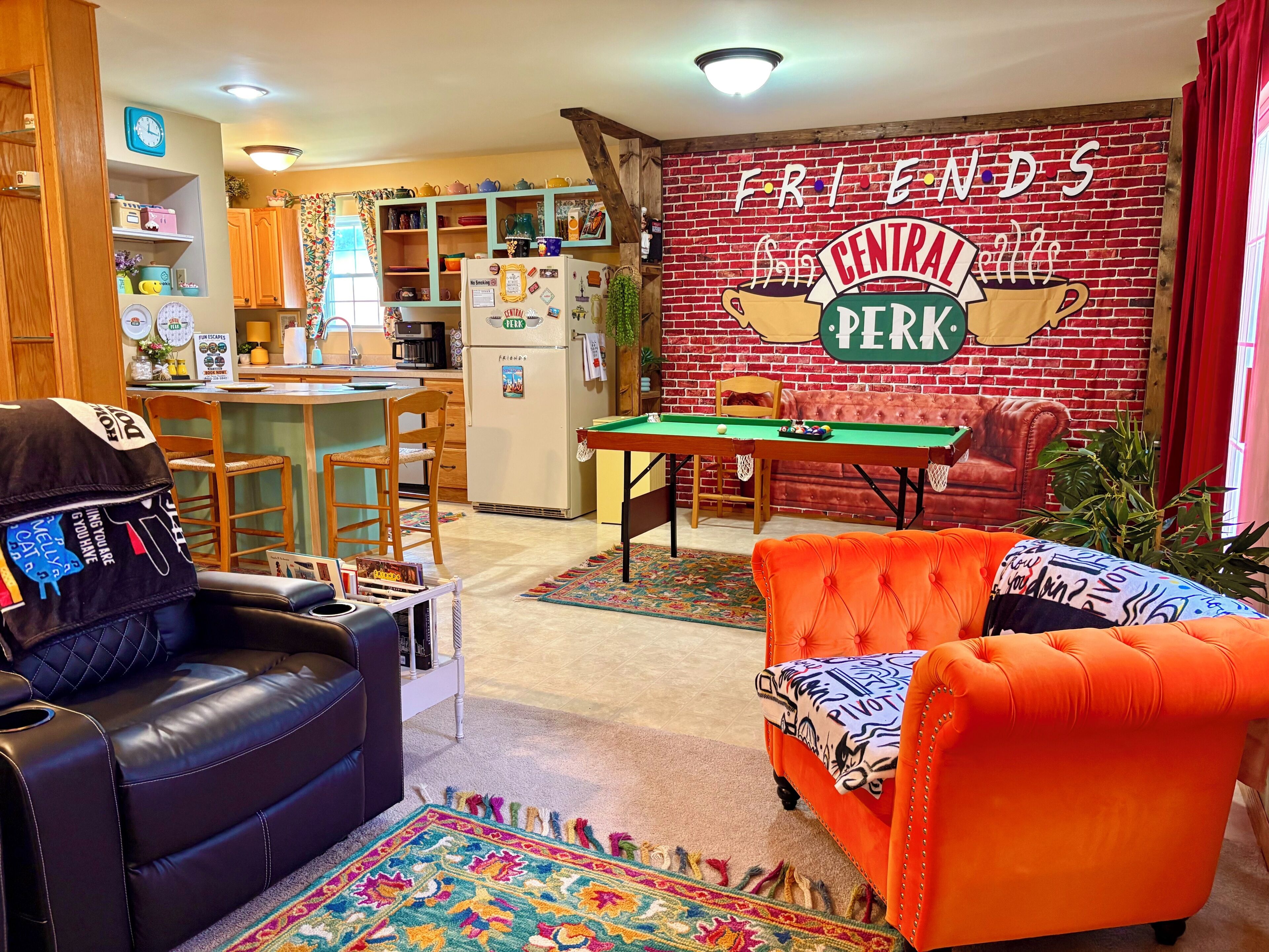 A cozy living room with a pool table, a sofa, and a kitchen area with a fridge and cabinets.