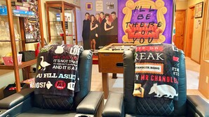 A room with two black leather chairs, a foosball table, and a wall decorated with 'Friends' posters. - “Friends” Central Perk- Fun Escape - Starved Rock- Ottawa (Ottawa)