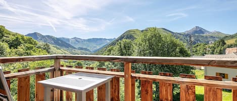 A wooden deck with a metal table, overlooking a mountainous landscape with lush greenery and distant peaks.