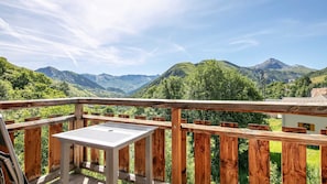 A wooden deck with a metal table, overlooking a mountainous landscape with lush greenery and distant peaks. - Apartment for 6 people, balcony with a view of the mountains (Saint-Sorlin-d´Arves)