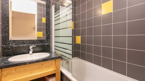 Un baño con lavamanos de mármol, cabina de ducha con mampara de vidrio y paredes de baldosas oscuras con detalles amarillos.