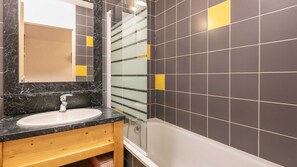 A bathroom with a marble sink, a glass shower enclosure, and dark tiled walls with yellow accents. - Apartment for 6 people, balcony with a view of the mountains (Saint-Sorlin-d´Arves)