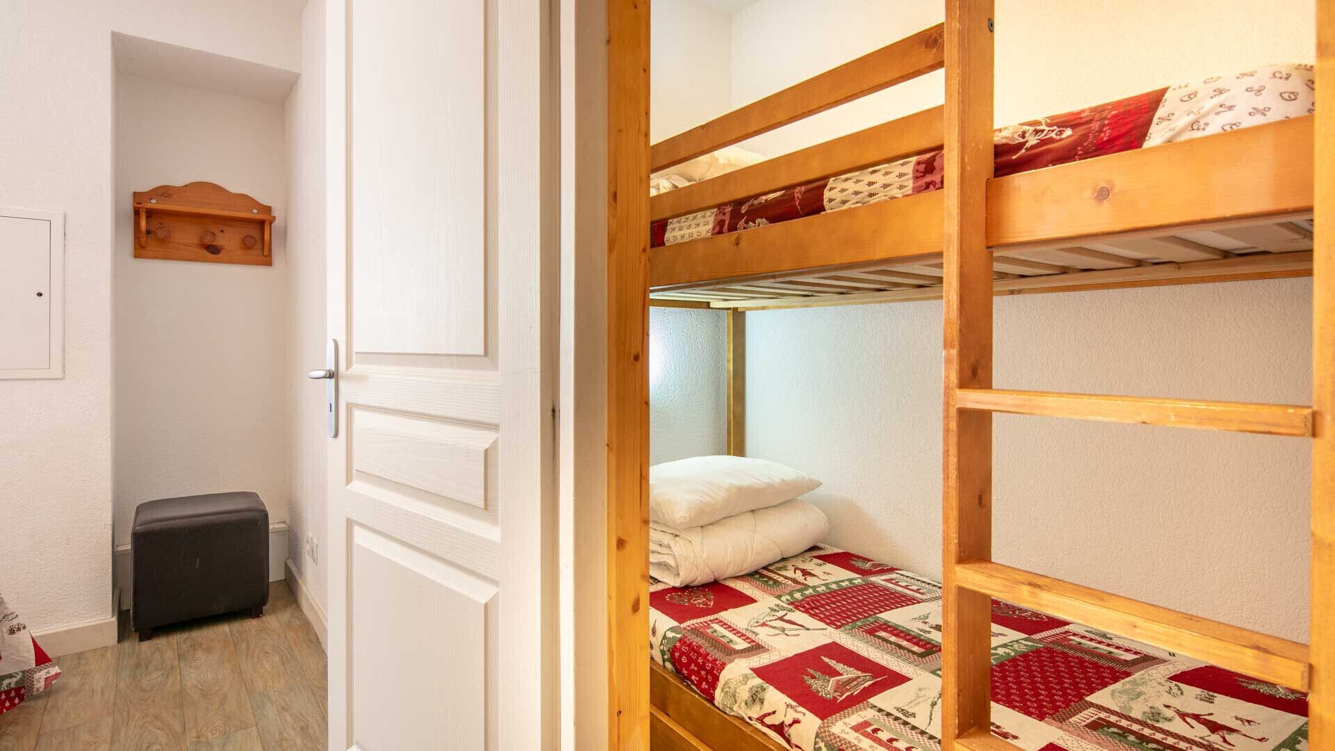 A room with a bunk bed, a small wooden shelf, a door, and a suitcase on the floor.
