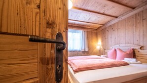A wooden cabin room with a bed, a window, and a door with a metal handle. - Golmerhaus (Tschagguns)