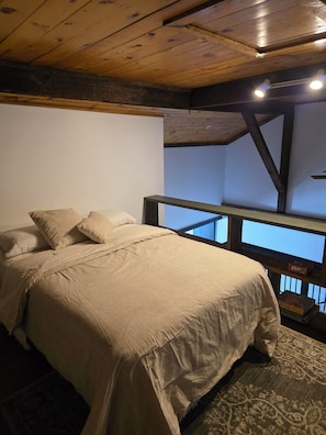 Un dormitorio con cama, vigas de madera en el techo, una mesita de noche y vistas al exterior.