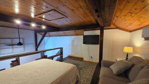 Ein Zimmer mit einem Bett, einem Sofa, einem an der Wand befestigten Fernseher und einem Deckenventilator.