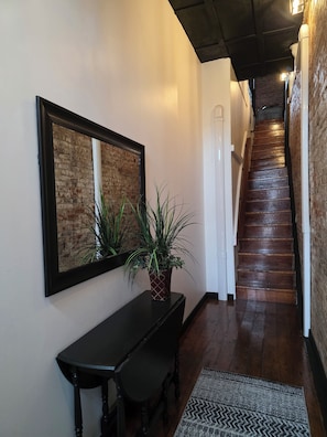 Un pasillo con una escalera, una obra de arte enmarcada en la pared, una planta en maceta y un banco de madera oscura.