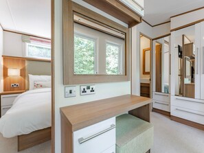 Ein modernes Hotelzimmer mit Bett, Nachttisch, Lampe, Spiegel und integriertem Kleiderschrank.