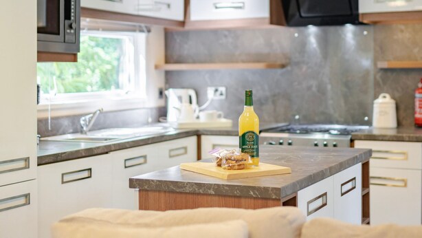 A modern kitchen with a microwave, stove, and a bottle of apple juice on the counter. - Fern View - Kelling Heath Holiday Park (Holt)
