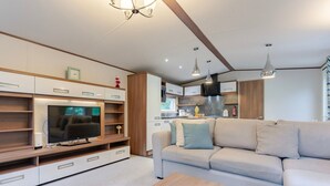 A modern living room with a flat-screen TV, wooden entertainment unit, beige sofa, and a coffee table. - Fern View - Kelling Heath Holiday Park (Holt)