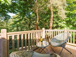 Eine Holzterrasse mit Korbstühlen und einem kleinen runden Tisch, umgeben von dichtem Baumbestand.