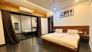 Quarto de hotel com uma cama grande, um ventilador de teto, um ar condicionado, uma mesa de cabeceira e uma obra de arte na parede.