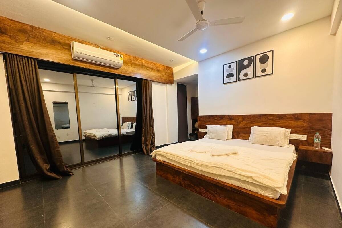 A hotel room with a large bed, a ceiling fan, an air conditioning unit, a nightstand, and a wall-mounted artwork.