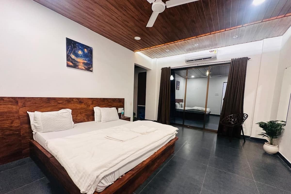 A modern hotel room with a wooden headboard, a large bed, a ceiling fan, a night sky painting, a potted plant, and a view of a bathroom.