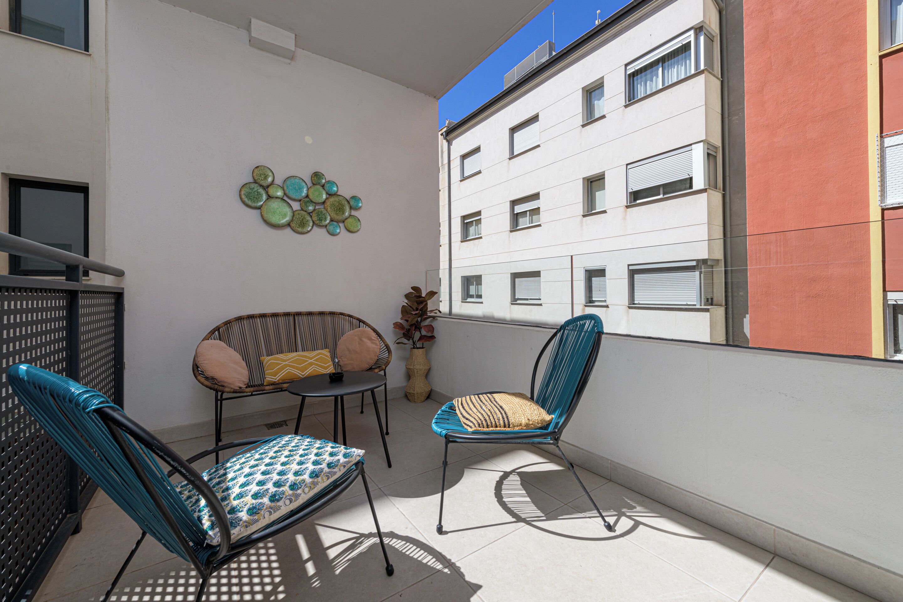Un balcón con dos sillas, una mesa pequeña y un adorno de pared con un plato decorativo.
