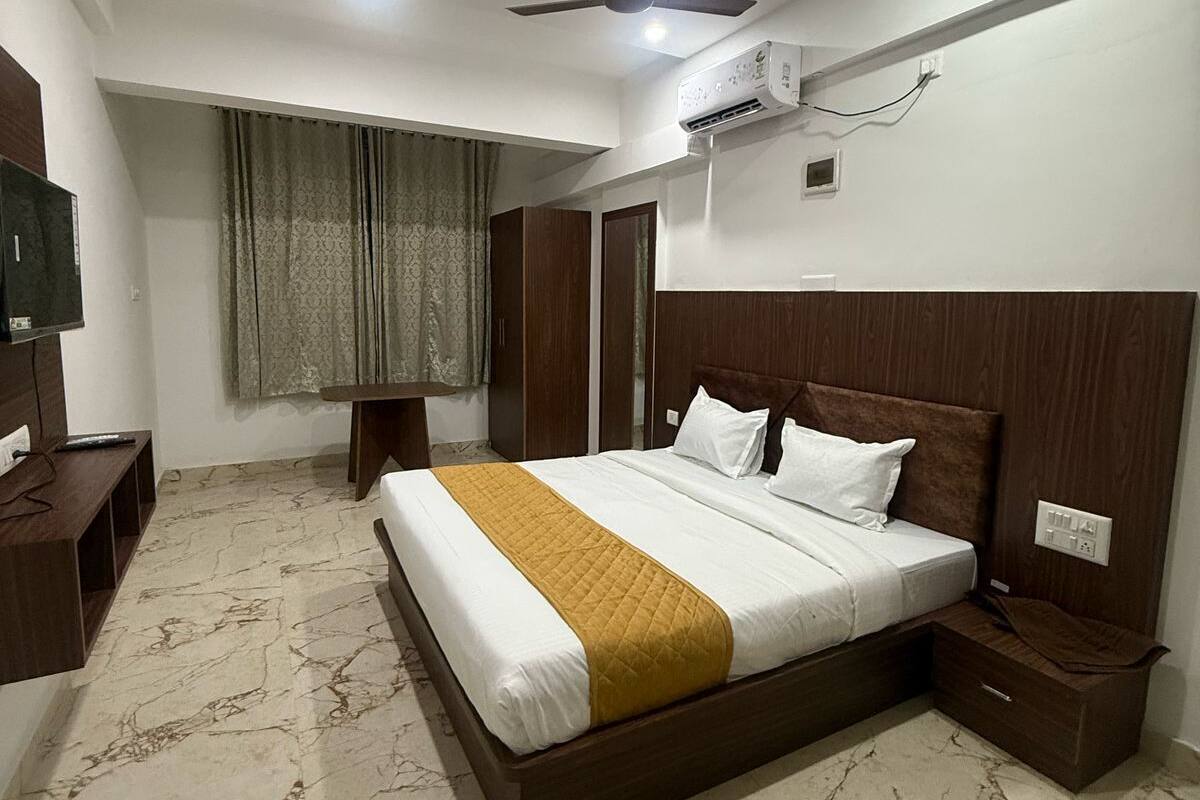 Habitación de hotel con cama, ventilador de techo, aire acondicionado, televisor y ventana con cortinas.