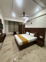 Habitación de hotel con cama, ventilador de techo, aire acondicionado, televisor y ventana con cortinas.