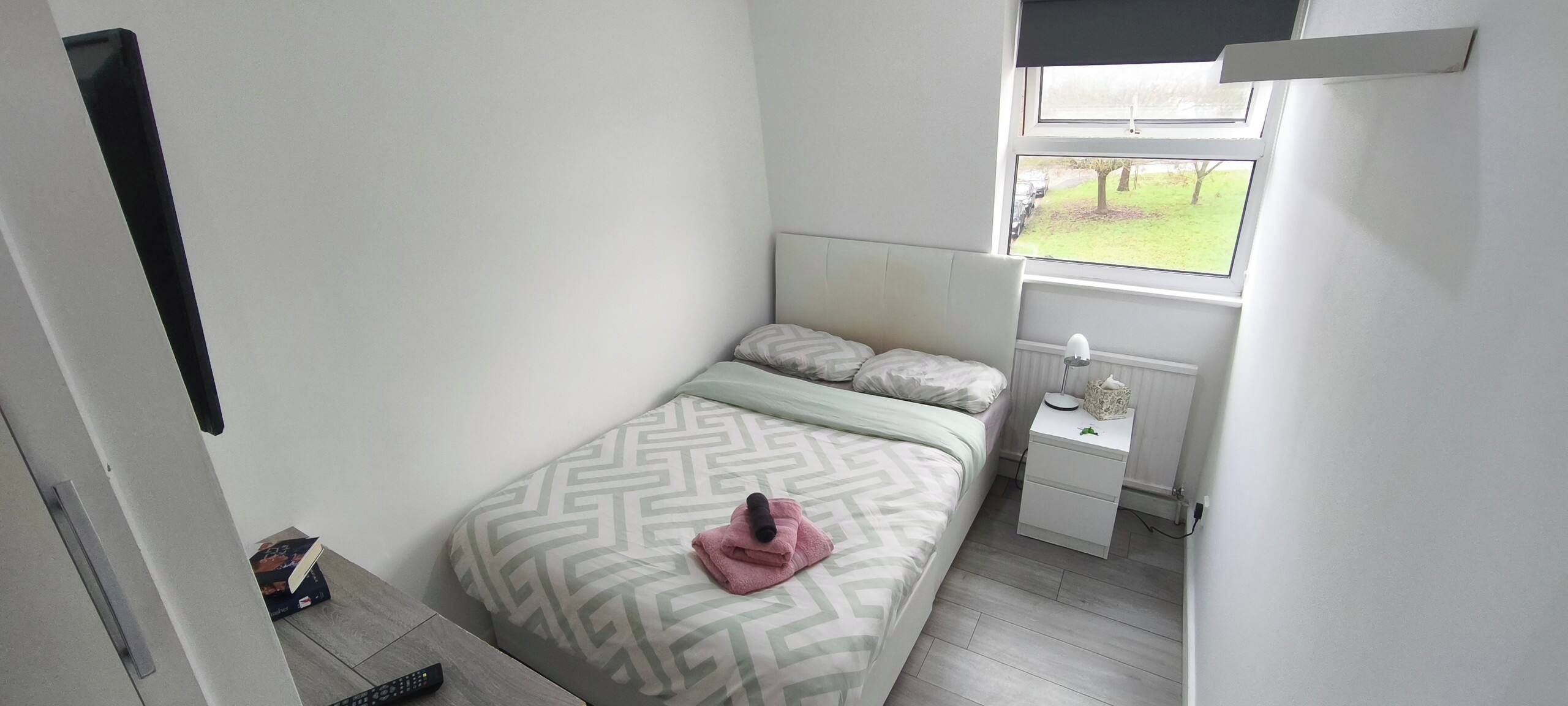 A bedroom with a bed, bedside table, and a window with a view.