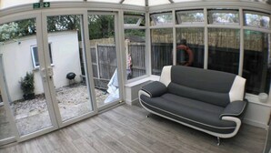 A conservatory with a sofa, glass doors, and a view of a backyard. - Room-cozy Small Room in City Centre and (Chelmsford)