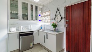 A kitchen with white cabinets, a dishwasher, a clock, and a wooden door. - The Quiet Hidden Gem (Johannesburg)