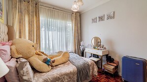 A bedroom with a bed, a dresser, a mirror, a teddy bear, and a suitcase. - The Quiet Hidden Gem (Johannesburg)