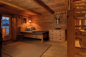 Een houten blokhut van binnen met een bed, een dressoir, een raam met uitzicht op de bergen en gewei aan de muur.