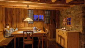 Interior de uma cabana de madeira com mesa de jantar, cadeiras, um banco, armário de madeira e cortinas xadrez.