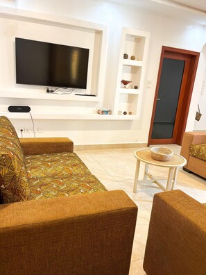 Ein Wohnzimmer mit flachbildfernseher an der Wand, einem Sofa, einem Couchtisch und einer Tür.