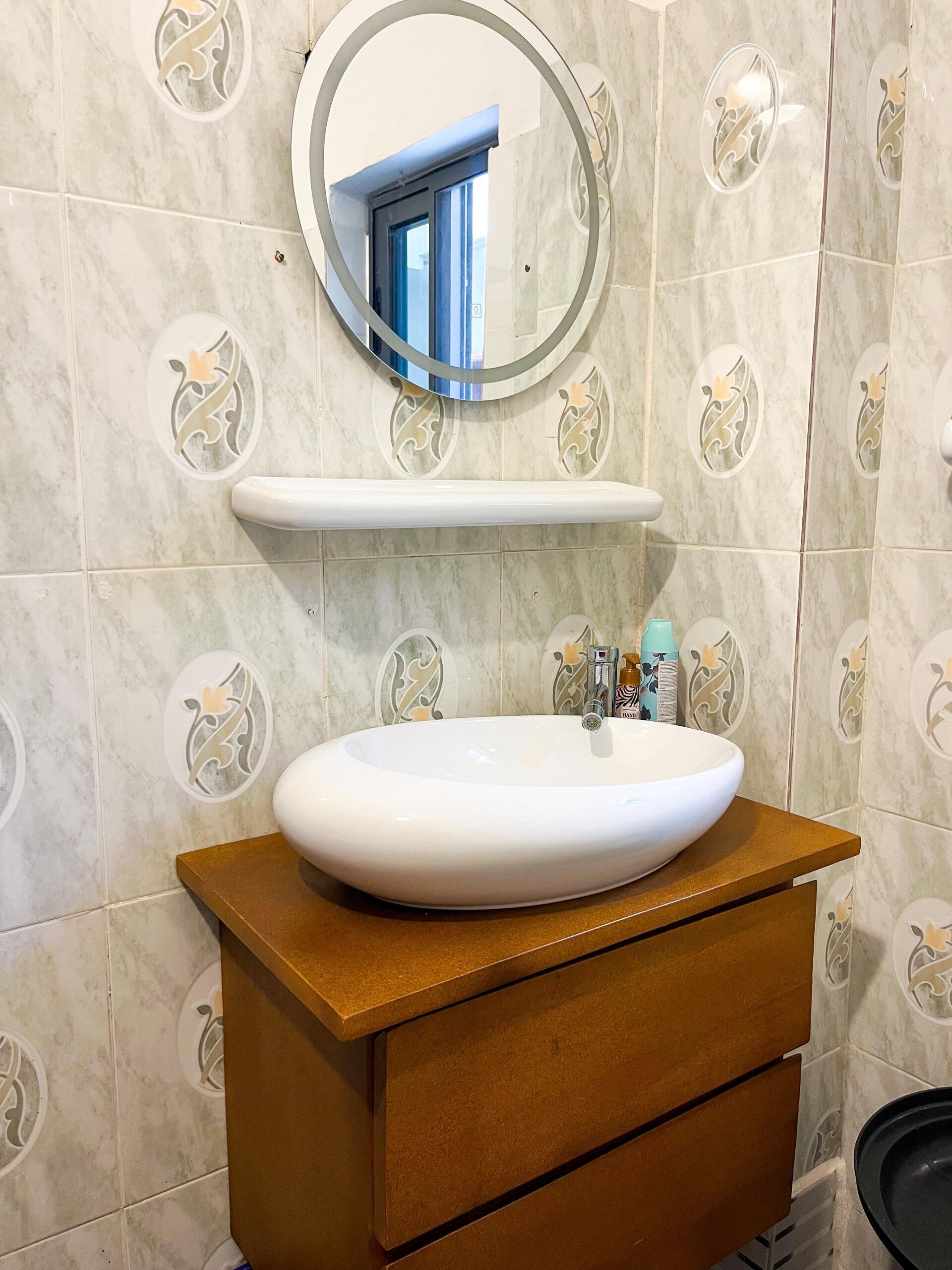 A bathroom with a white sink, a mirror, a shelf, and patterned tiles.