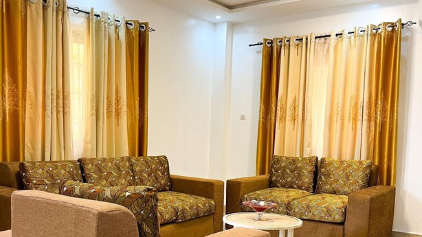 Ein Wohnzimmer mit zwei Sofas, einem Couchtisch und Vorhängen mit Blätermotiv.
