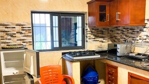 Eine Küche mit Fenster, Schränken, einer Mikrowelle, einem Gasherd und einem Mülleimer.