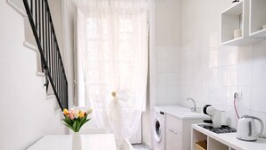 Una cocina compacta con lavadora, una mesa de comedor con un florero y estanterías blancas.