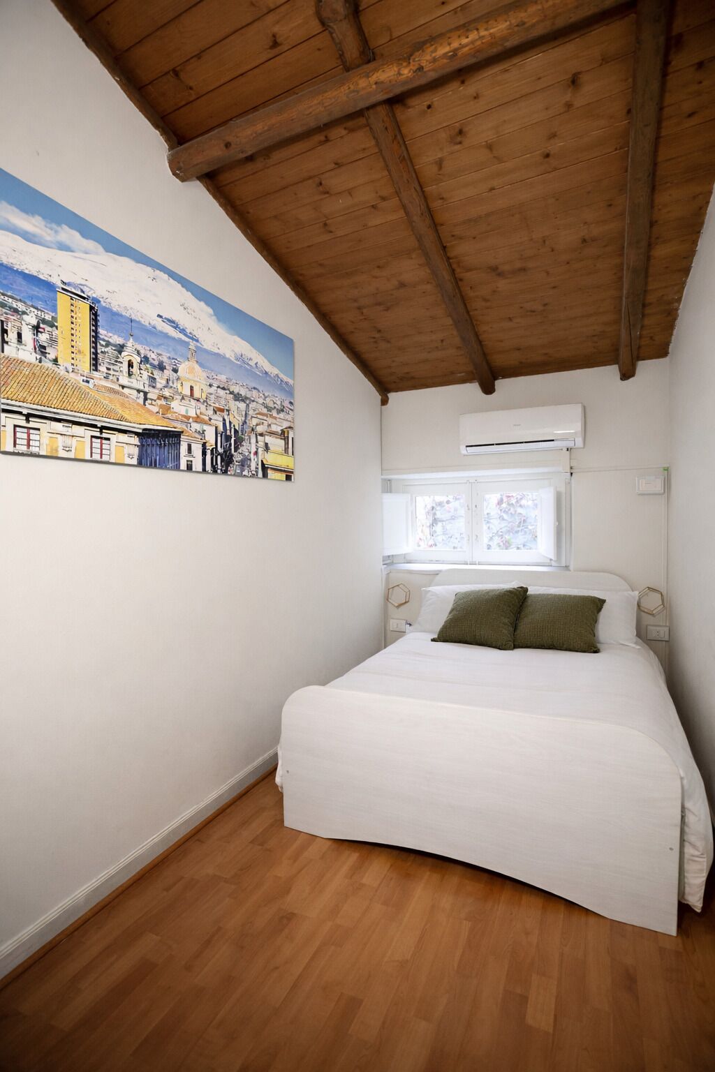 A bedroom with a wooden ceiling, a bed with white bedding, a wall-mounted air conditioner, and a window with a view of a snowy landscape.