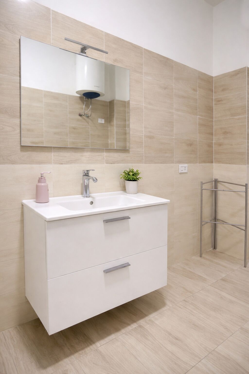 A modern bathroom with a white vanity, a mirror, a small potted plant, and a shower area.