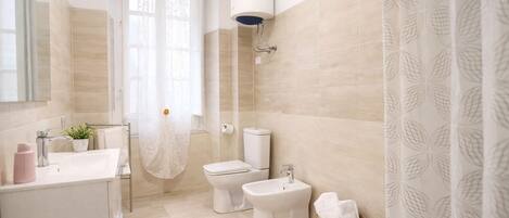 A bathroom with a toilet, bidet, sink, and a shower area.