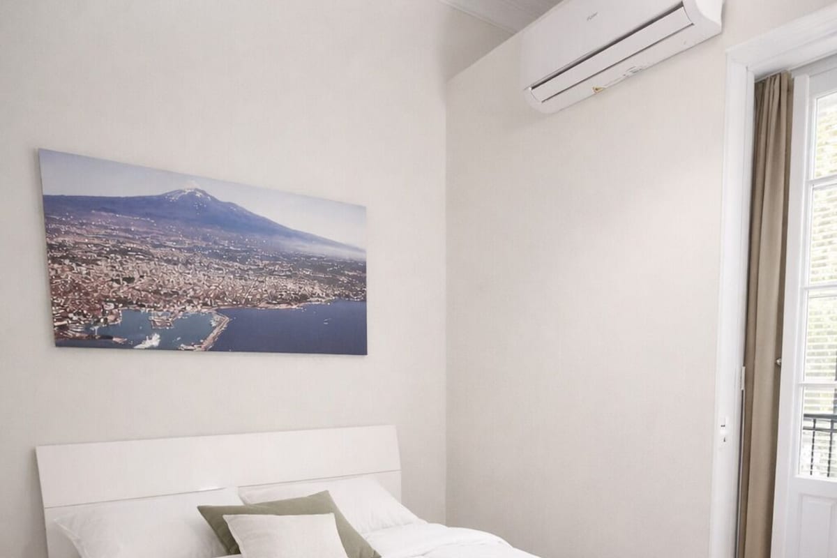 Una camera da letto con un letto, un poggiapiedi rotondo, un quadro che raffigura un panorama urbano e un condizionatore d'aria.