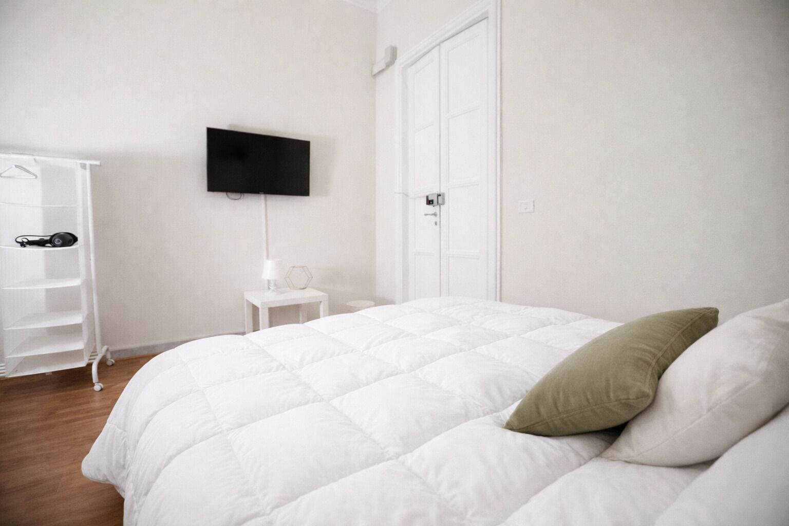 Une chambre à coucher comprenant un lit, un téléviseur fixé au mur, une armoire et une petite table de chevet avec une lampe.