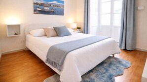 Un dormitorio con cama, mesitas de noche, cortinas en una ventana y un cuadro en la pared.