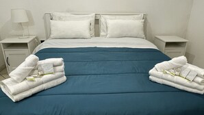 Una cama bien hecha con una colcha azul, almohadas blancas y dos toallas blancas dobladas a cada lado.