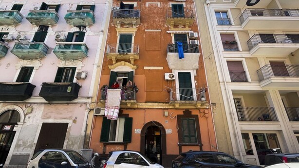 Una hilera de edificios de varios pisos con balcones y unidades de aire acondicionado, y una calle al frente.