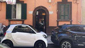 Un edificio con una puerta que indica 'VENDESI' y dos coches estacionados frente a él.