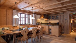 A wooden interior with a dining table, chairs, a kitchen area, and a staircase. - Berghaus Gauertal (Tschagguns)