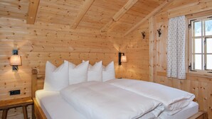A wooden cabin room with a bed, wall-mounted lamps, and a window with curtains. - Berghaus Gauertal (Tschagguns)