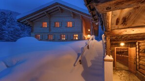 A log cabin with a snow-covered exterior, a wooden porch, and a lit entrance. - Berghaus Gauertal (Tschagguns)