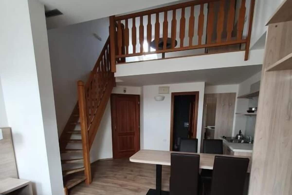 Habitación de hotel con cama, escritorio, silla, escalera y kitchenette.