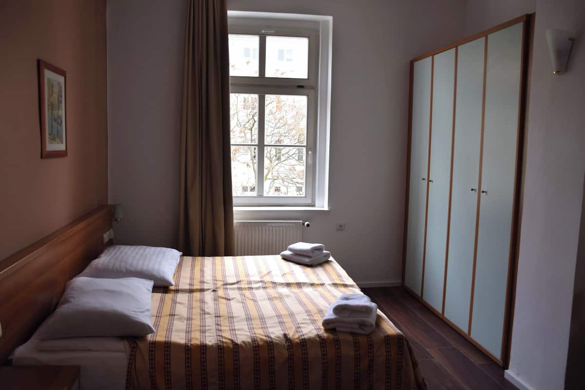 Un dormitorio con cama, ventana, radiador, armario y un cuadro en la pared.